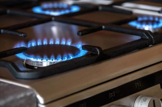 Două arzătoare de aragaz aprinse cu flacără albastră de gaz natural, prim-plan pe plită