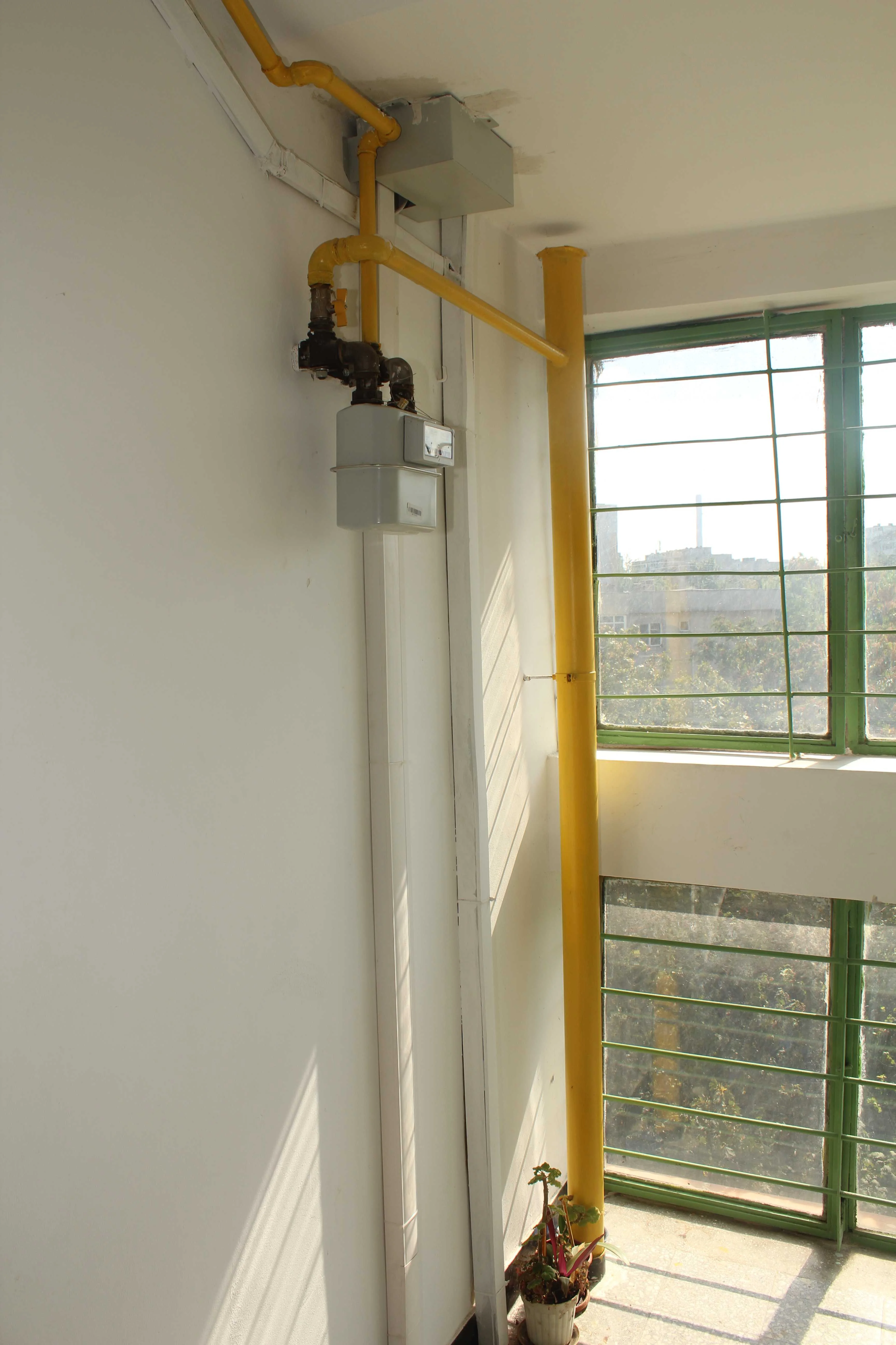 Contor de gaz si teava galbena montate pe perete, langa o fereastra