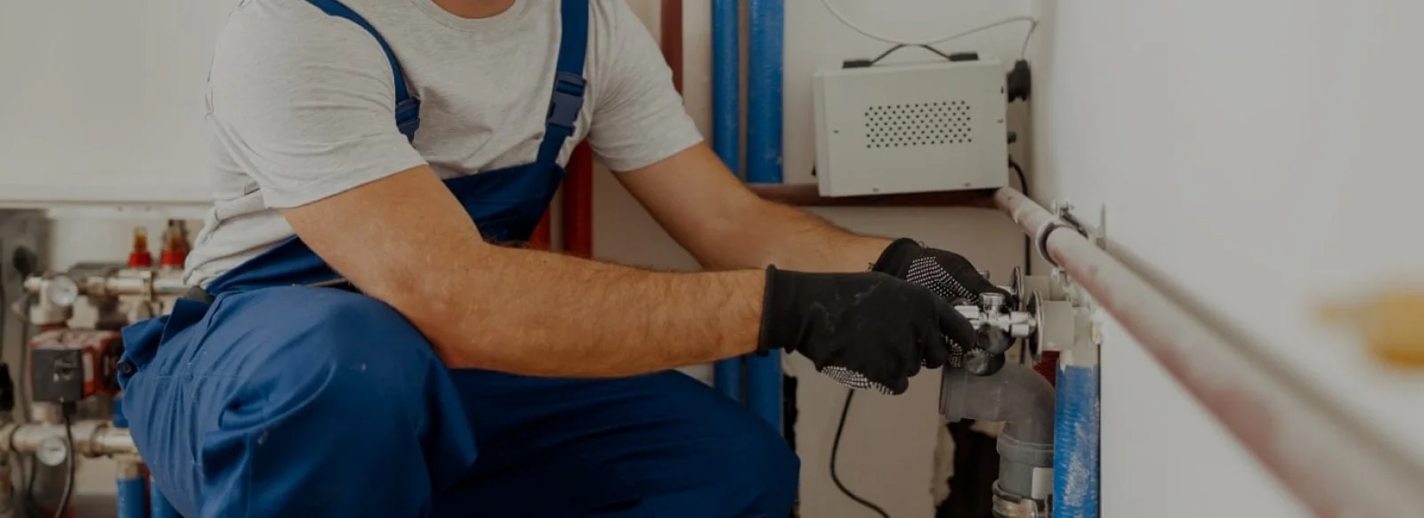 Instalator de gaze în salopetă albastră strânge un robinet la instalația de lângă centrala termică.