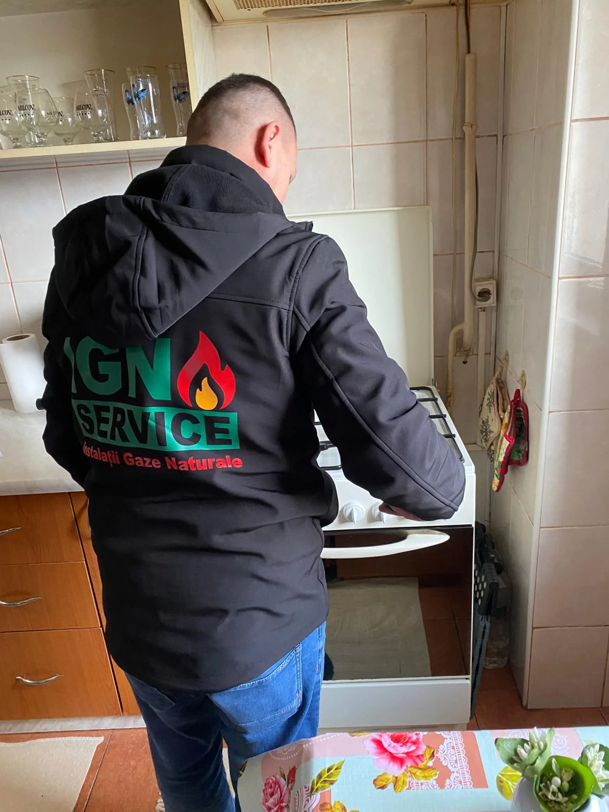 Instalator IGN Service lucrează la un aragaz alb pe gaz, cu ușa cuptorului deschisă, în bucătărie