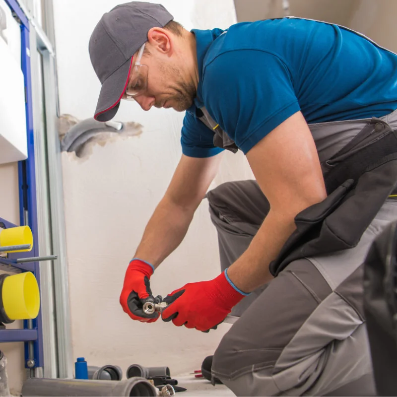Instalator IGN Service montează un fiting de instalație, echipat cu mănuși de protecție și unealtă de mână