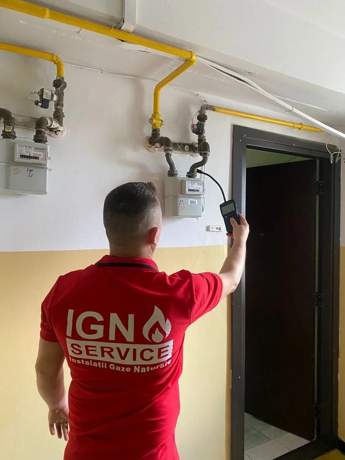 Instalator IGN Service verifică un contor de gaz cu detector electronic de scăpări lângă ușă