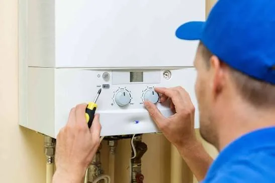 Tehnician reglează cu o șurubelniță butoanele unei centrale termice pe gaz montate pe perete