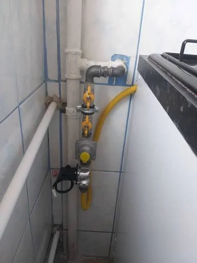 Robinet de gaz galben și furtun flexibil racordate pe perete faianțat, lângă un aparat