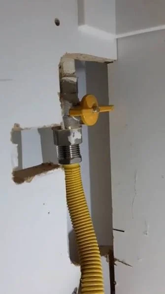 Robinet de gaz galben pe perete cu furtun flexibil ondulat pentru racordul aparatului