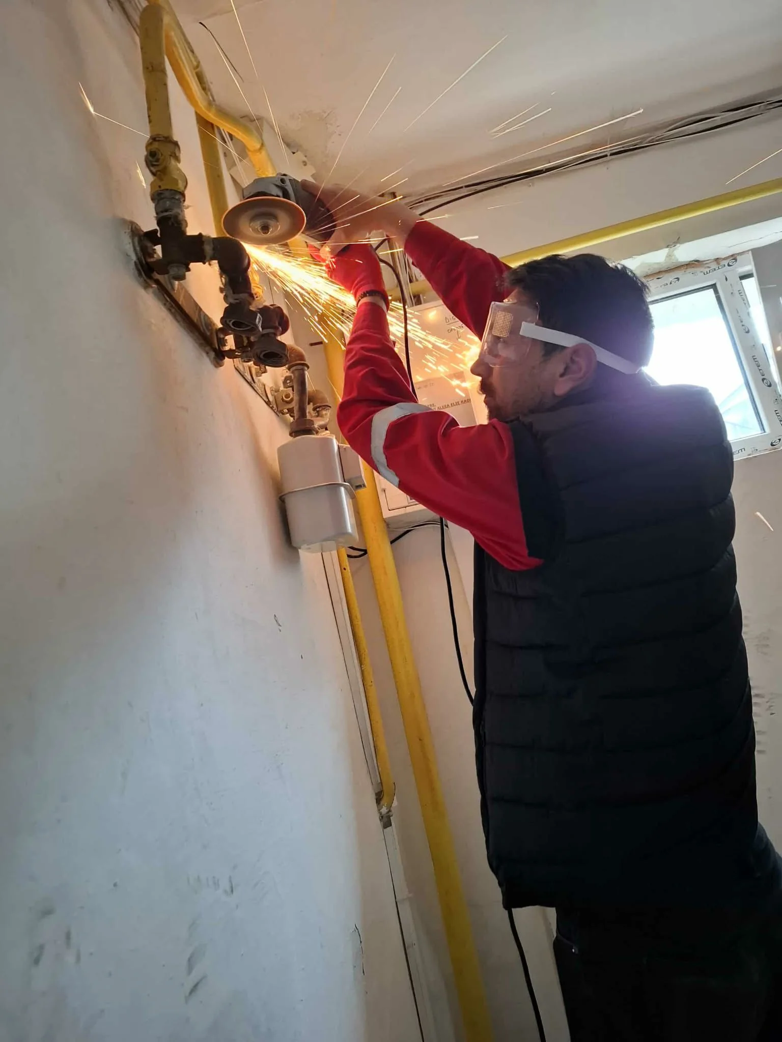 Instalator cu ochelari de protecție taie cu polizorul unghiular o țeavă galbenă de gaz, scântei