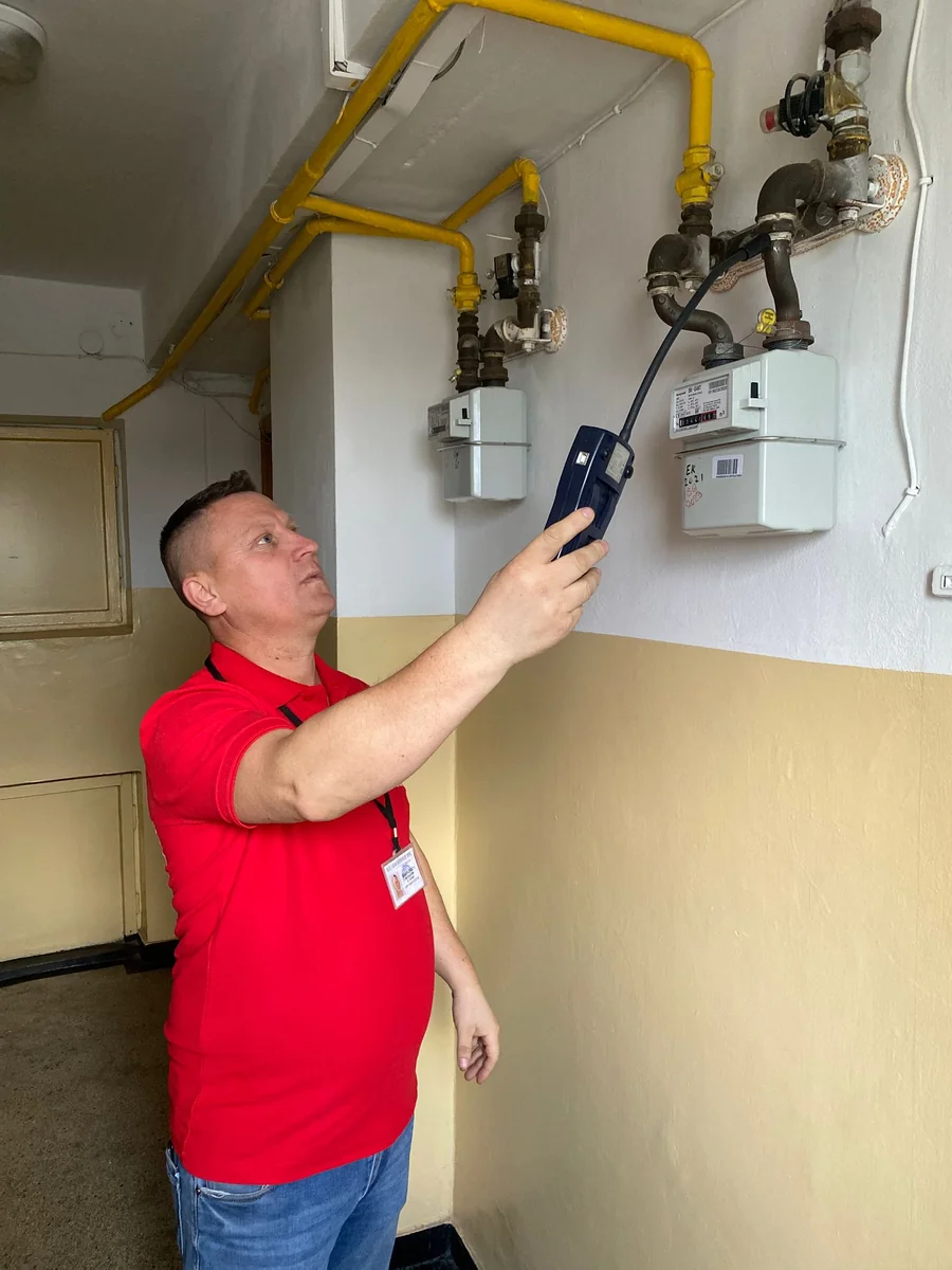 Tehnician IGN Service verifică cu detector electronic contoarele de gaz de pe holul unui bloc