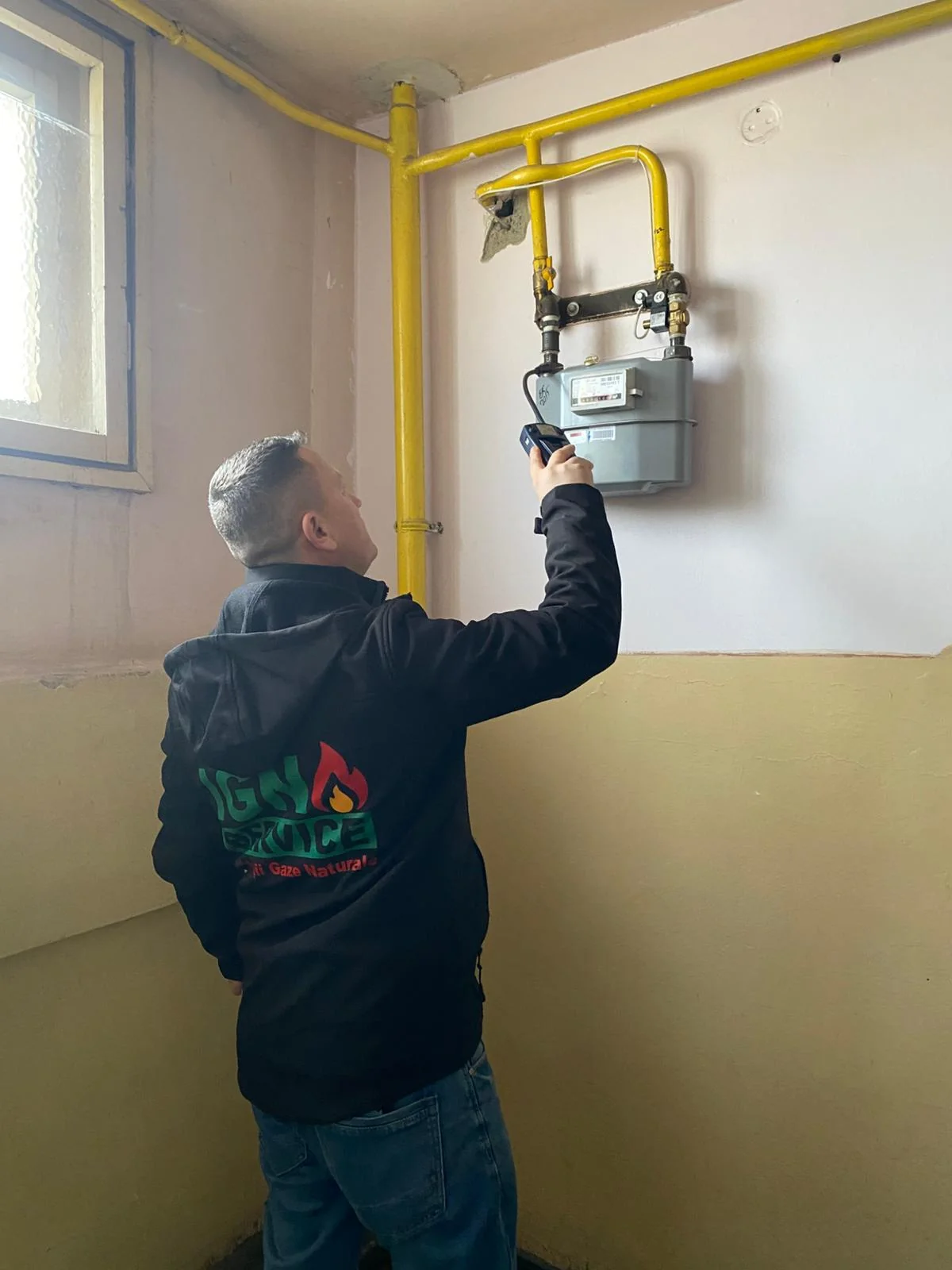 Tehnician IGN Service verifică contorul de gaz cu un detector portabil, lângă țevile galbene