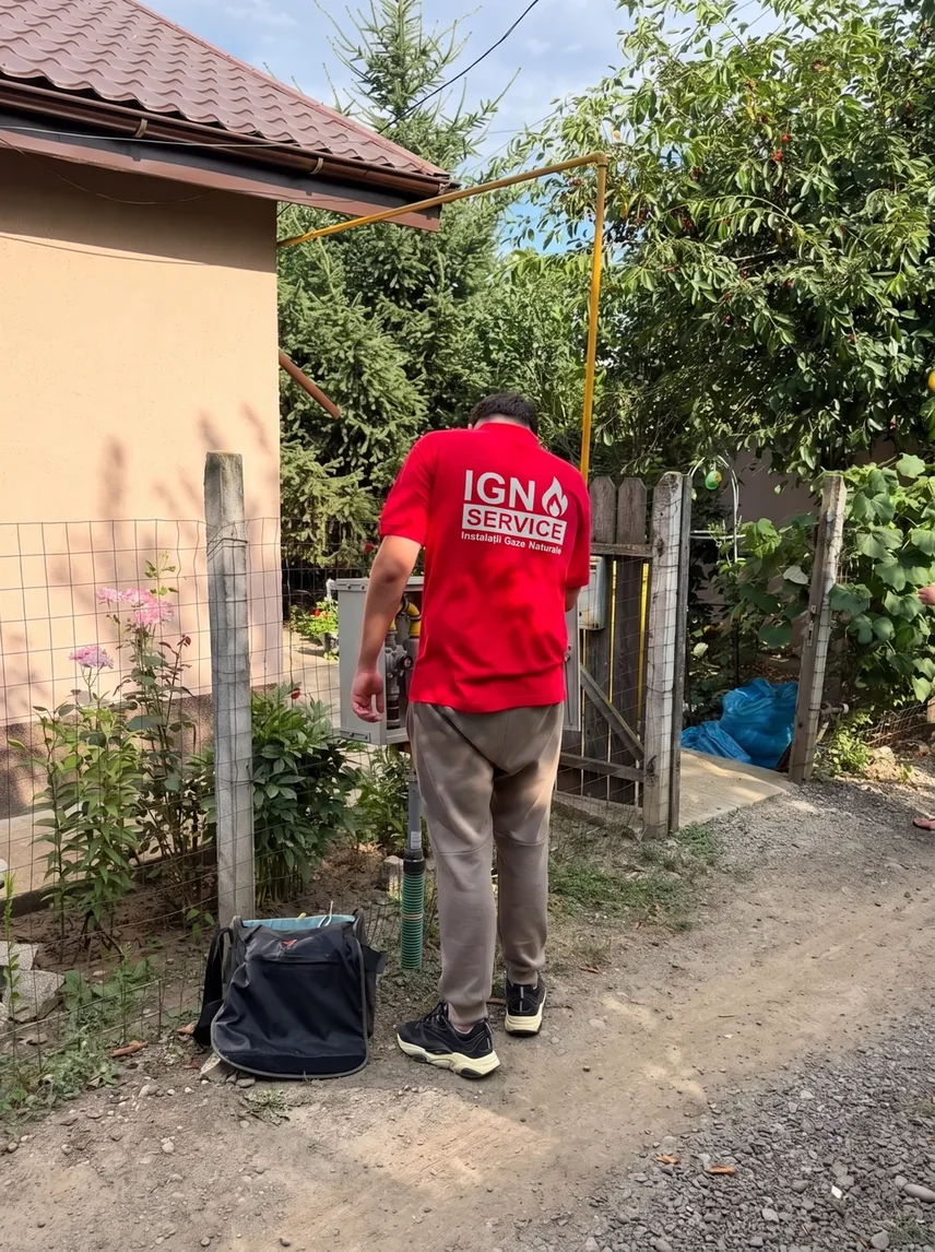 Instalator IGN Service lângă țeava galbenă de branșament gaz, la poarta unei case, cu geanta de scule