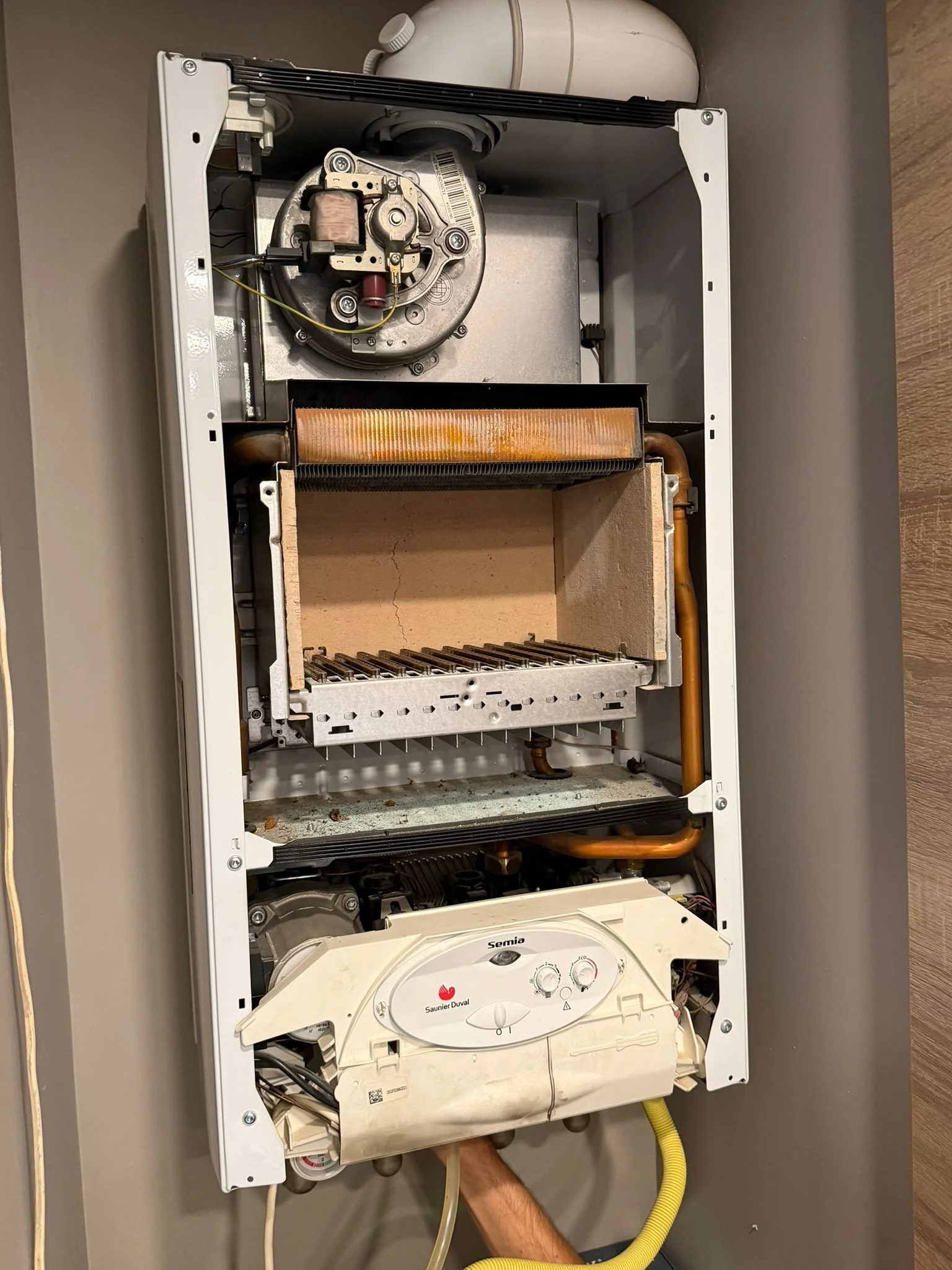 Instalator IGN Service deschide cu șurubelnița panoul frontal al unei centrale termice pe gaz