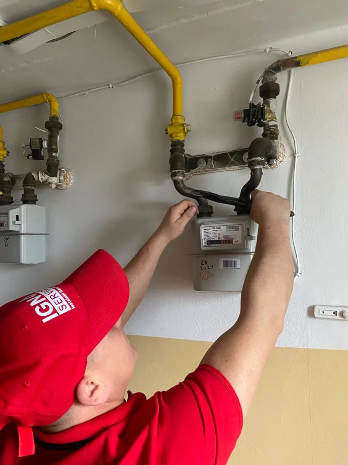 Mâinile unui instalator IGN Service strâng racordurile filetate ale unui contor de gaz de bloc