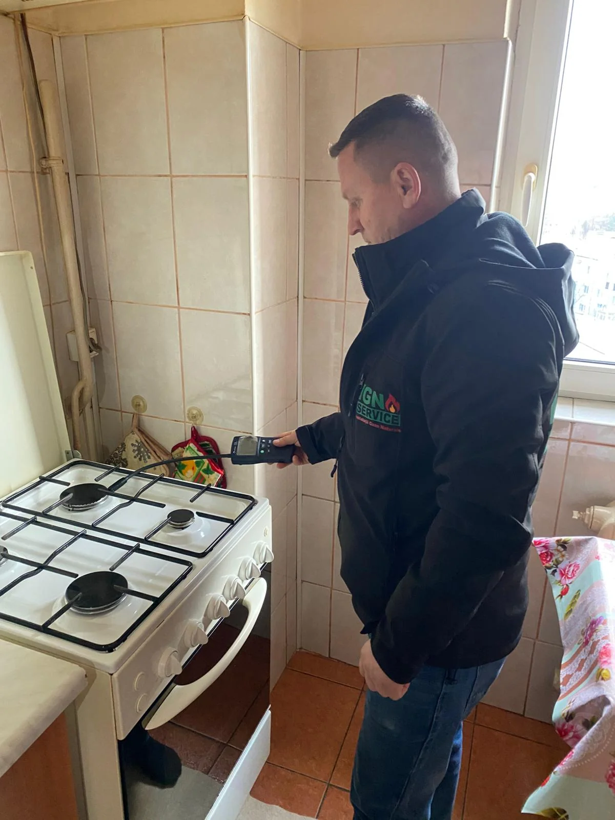 Tehnician IGN Service apropie detectorul portabil de aragazul alb cu patru arzătoare din bucătărie