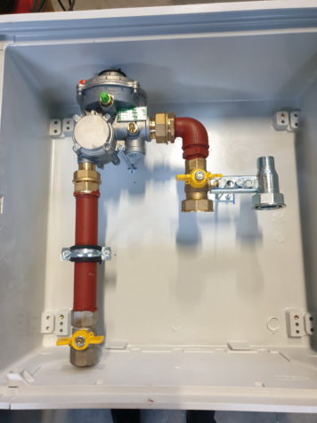 Regulator de presiune gaz într-o firidă cu țevi roșii, fitinguri și robinete galbene