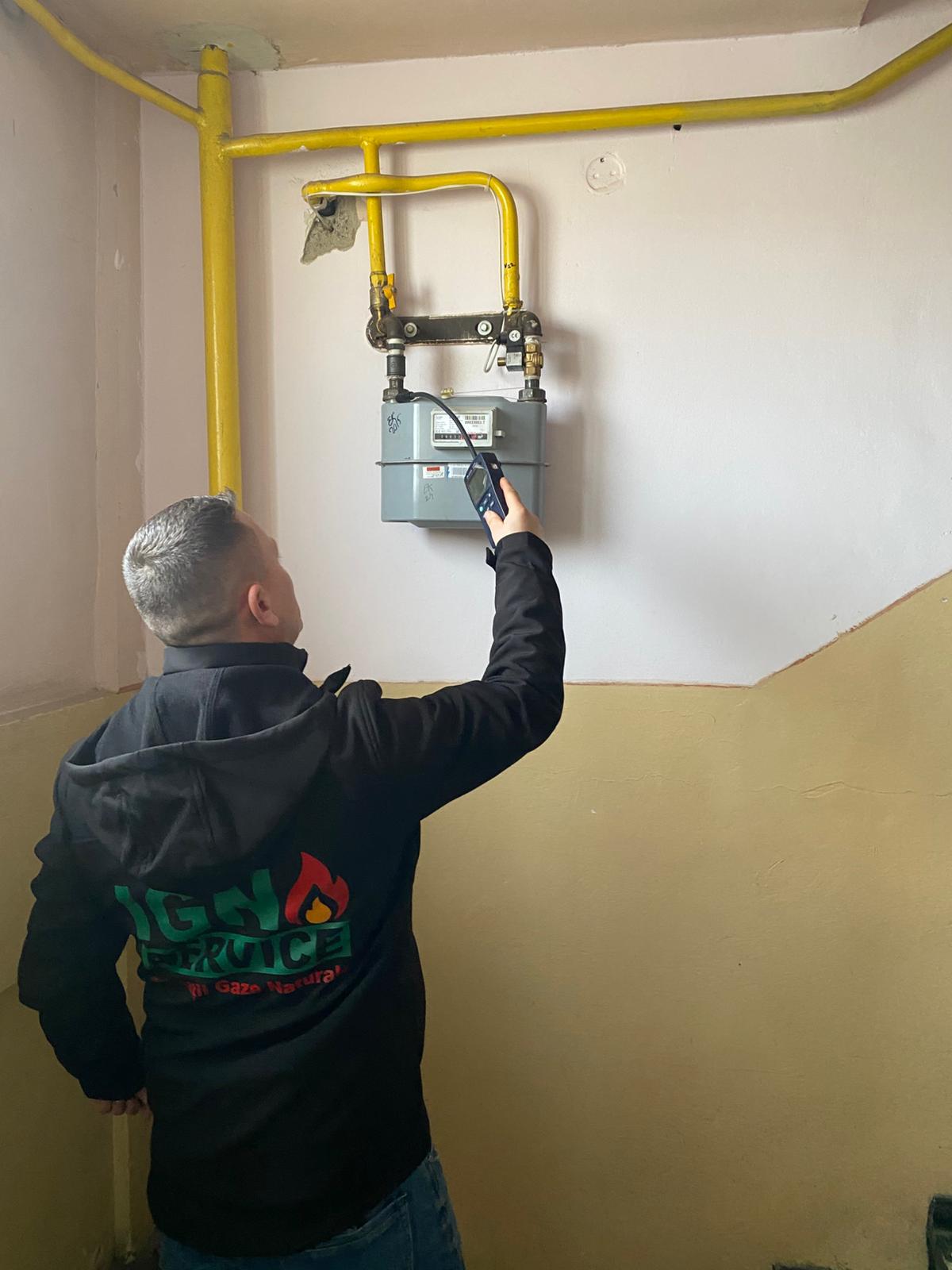 Tehnician IGN Service verifică contor de gaz cu detector electronic portabil, țevi galbene